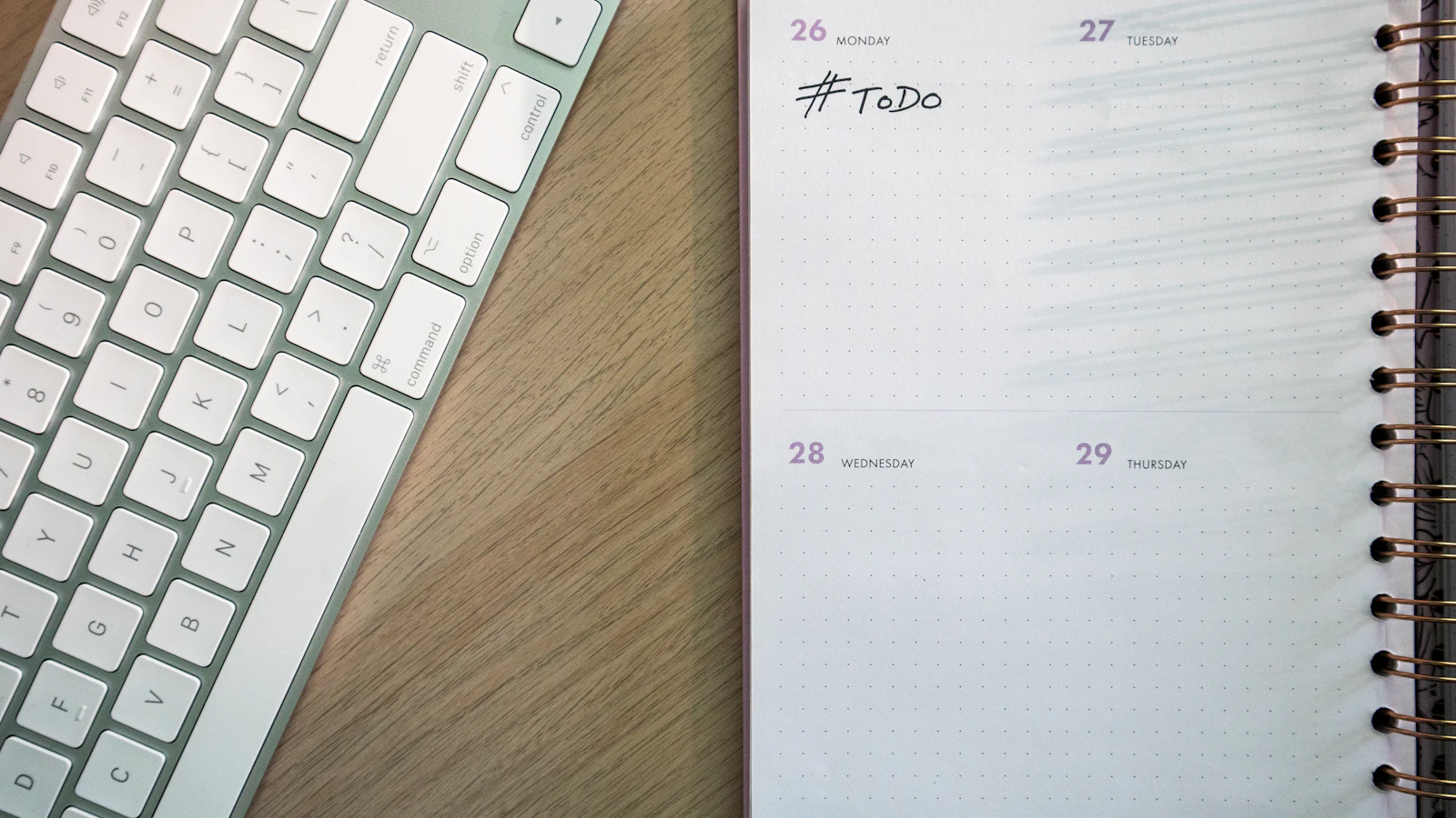 A weekly paper planner with #ToDo written under Monday, lying open on a wooden desk next to a white keyboard
